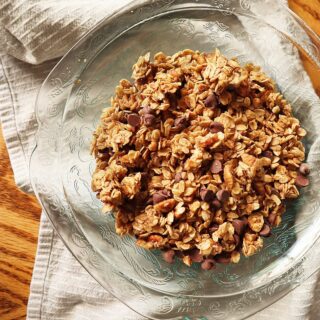 Photo of glass bowl with quick skillet granola on a wood table with a gray striped kitchen towel.