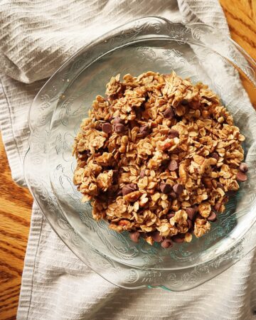 Photo of glass bowl with quick skillet granola on a wood table with a gray striped kitchen towel.
