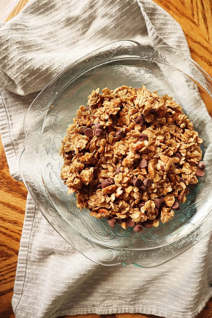 Photo of glass bowl of skillet granola on a striped kitchen towel on wood table.