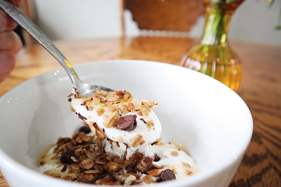 Woman holding spoon of instant pot greek yogurt with granola topping