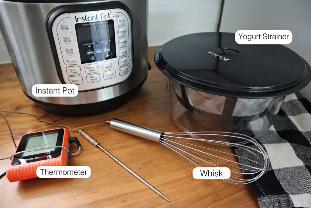 All the items needed to make instant pot greek yogurt and each of them are labeled: Instant pot, yogurt strainer, whisk, and thermometer