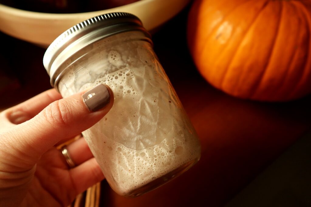 Woman's hand holding a small mason jar with foamy snickerdoodle creamer.